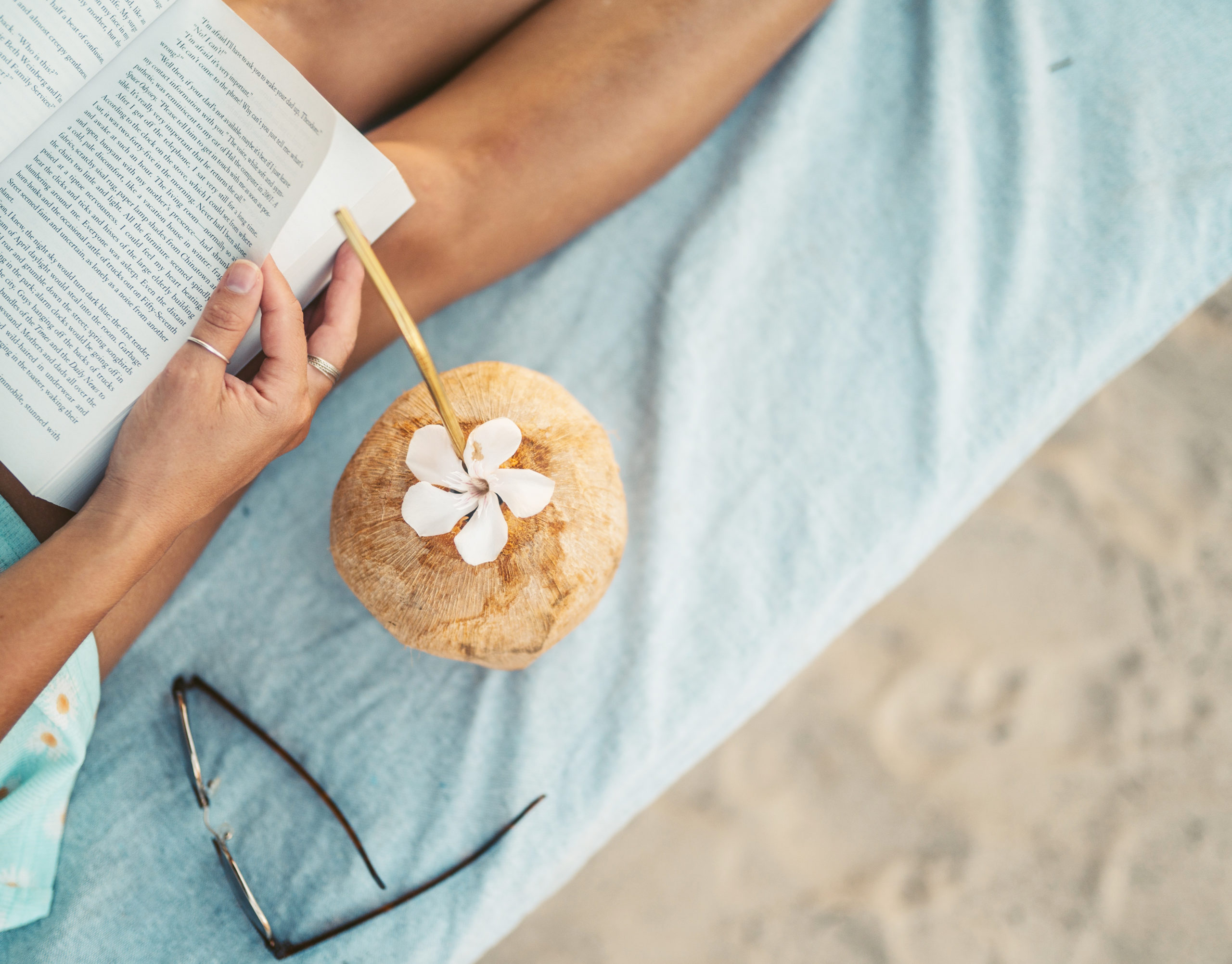 The 5 Essentials Every Entrepreneur Needs for an Unplugged Vacation - woman on a beach with a book and a coconut drink