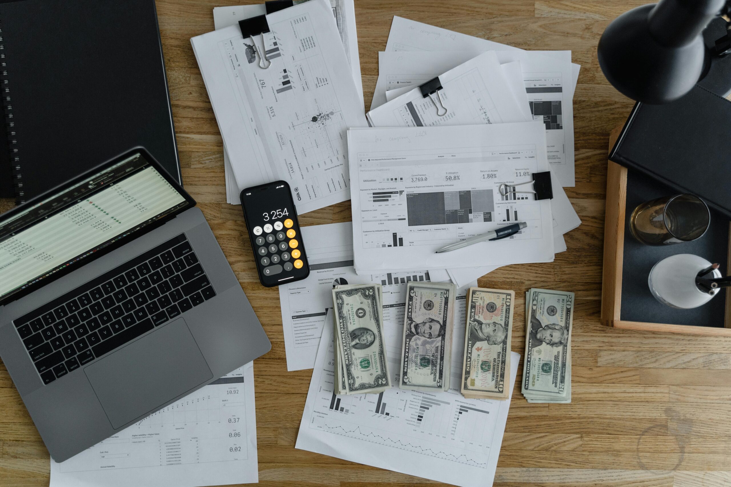 Laptop with financial charts, calculator, cash money, and business documents on wooden desk representing predictable revenue streams for creative entrepreneurs