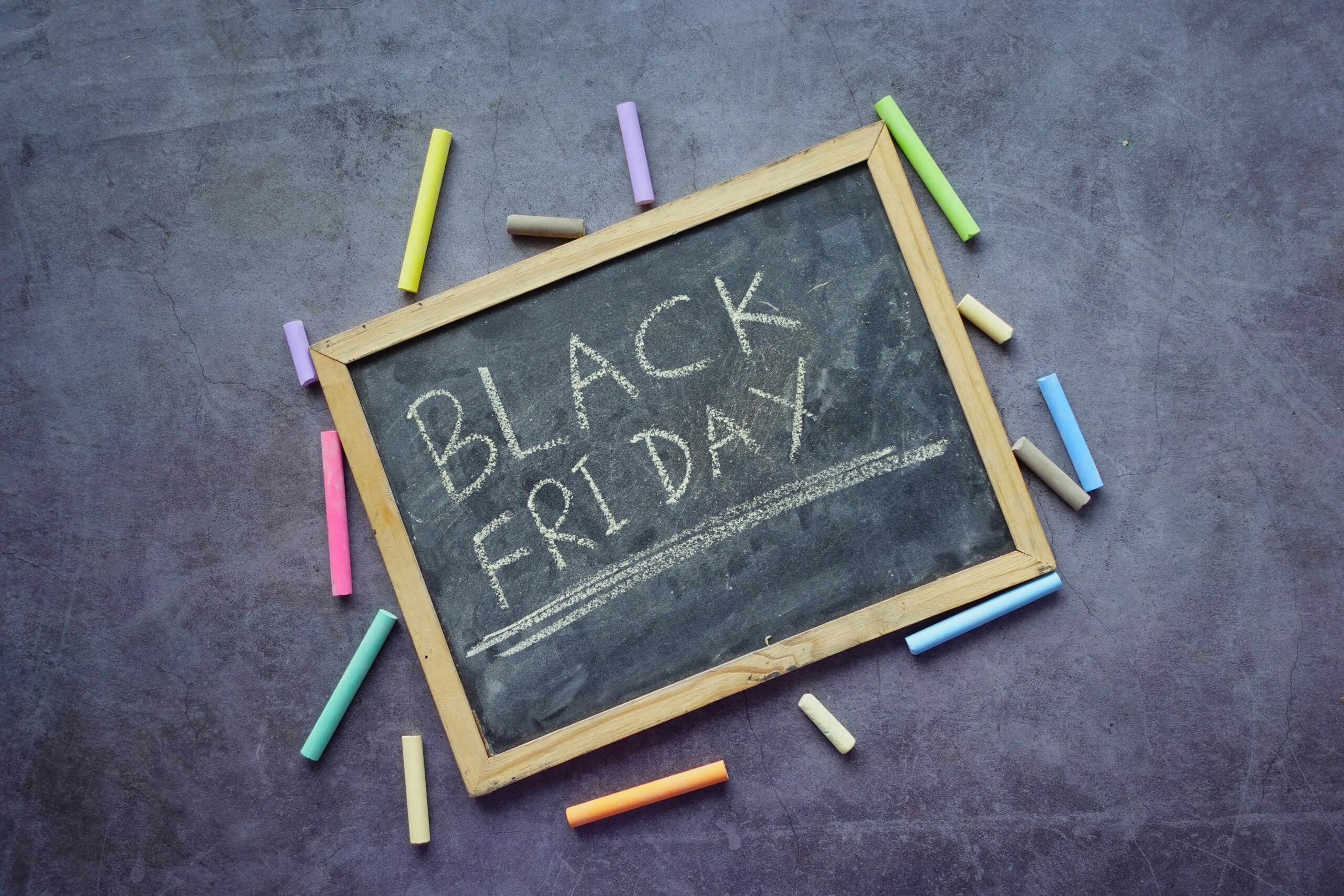 Black Friday text written in chalk on slate chalkboard surrounded by colorful chalk pieces for holiday marketing strategies blog