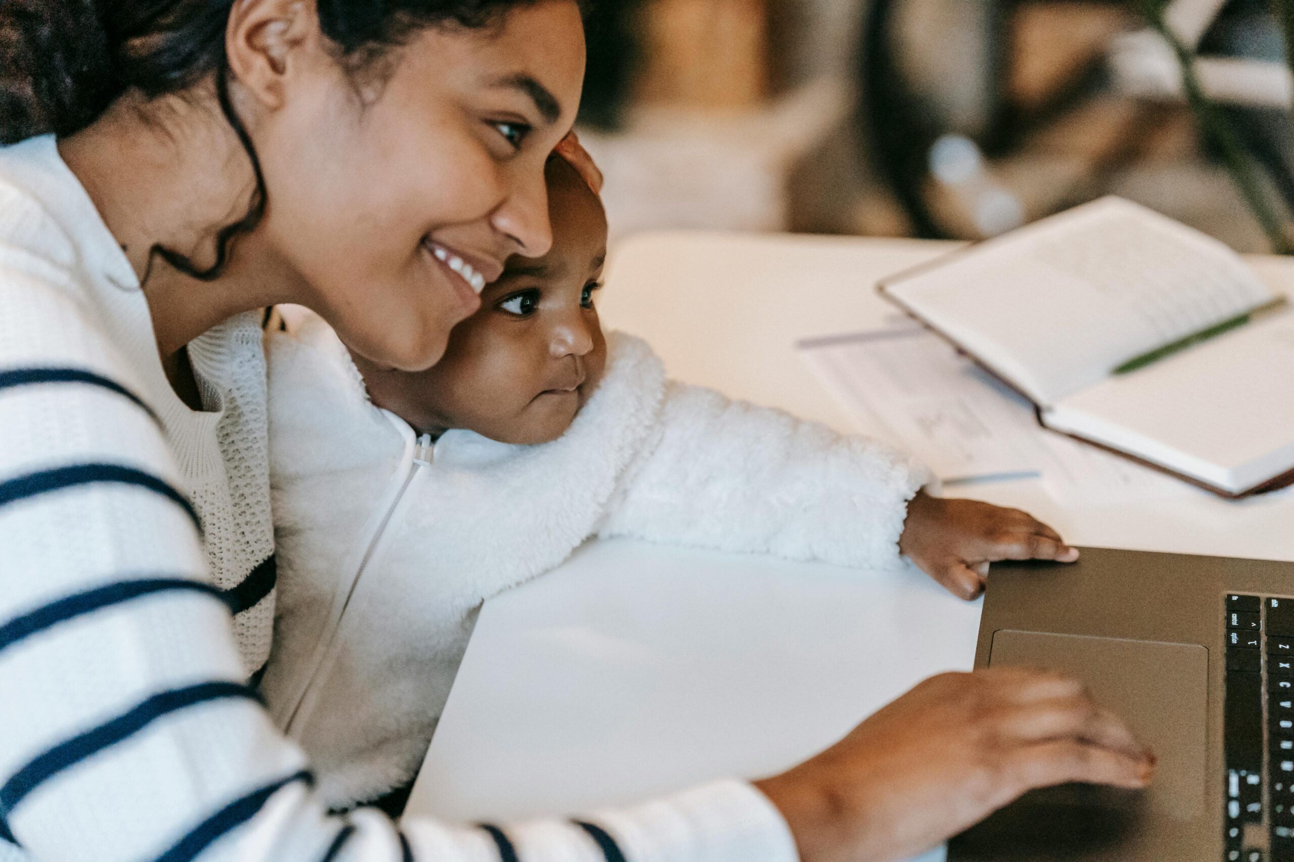 Smiling mom entrepreneur working on laptop with young child, demonstrating work-life balance and setting healthy boundaries while running a business from home